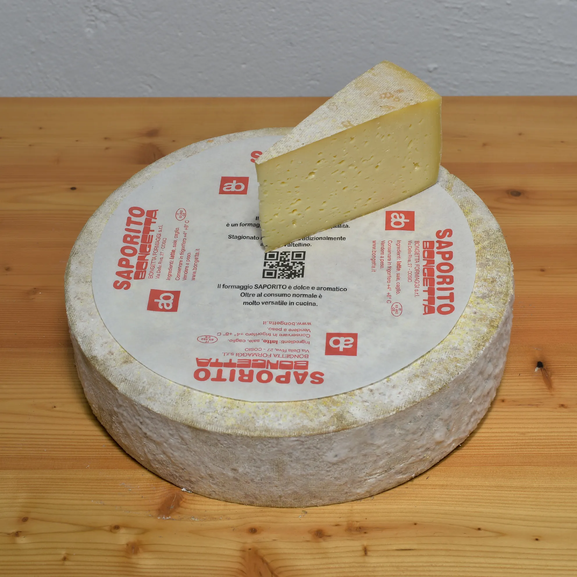 Wheel of Saporito on Bongetta Formaggi’s printed paper; the cut wedge shows straw-colored paste with scattered eyes.